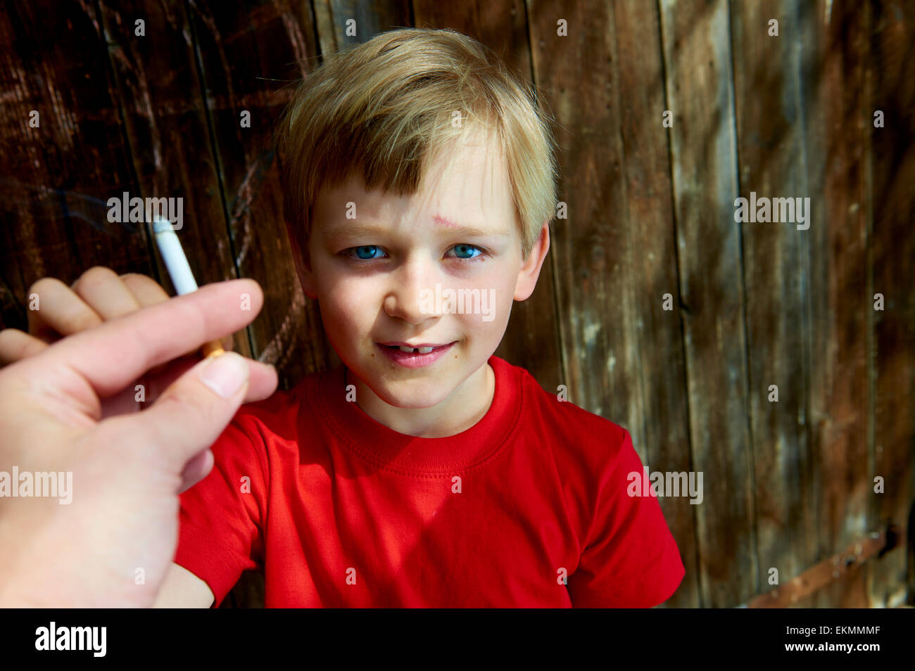 Ritratto di bambino biondo ragazzo Sigaretta fumare con legno scuro sfondo dietro di lui. Adult man mano che offre una sigaretta a boy Foto Stock