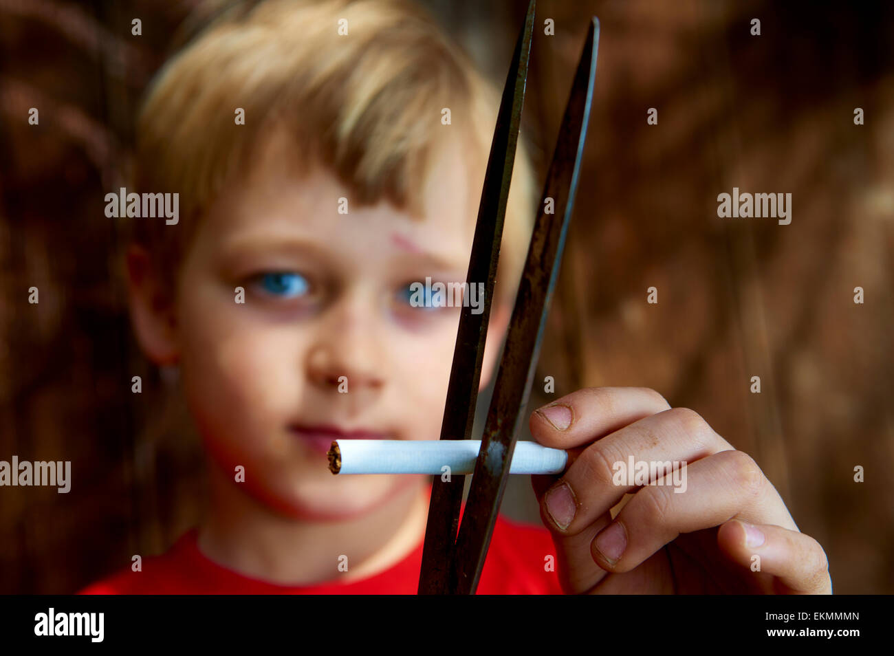 Close up bambino ragazzo biondo sigaretta di taglio con forbici e pareti in legno sfondo Foto Stock