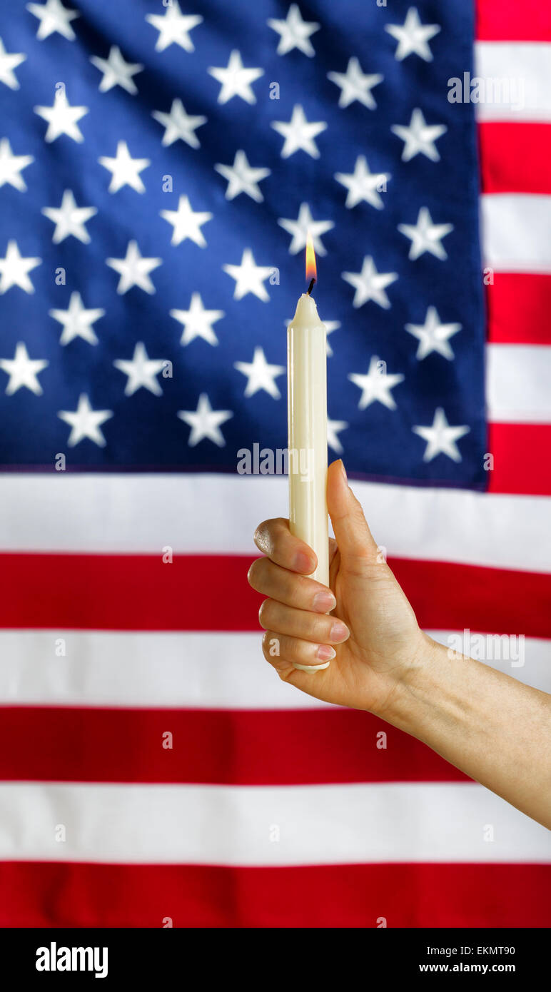 Chiudere verticali su immagine di una femmina di mano che tiene una sola candela bianca e luminosa fiamma con gli Stati Uniti d'America bandiera in b Foto Stock
