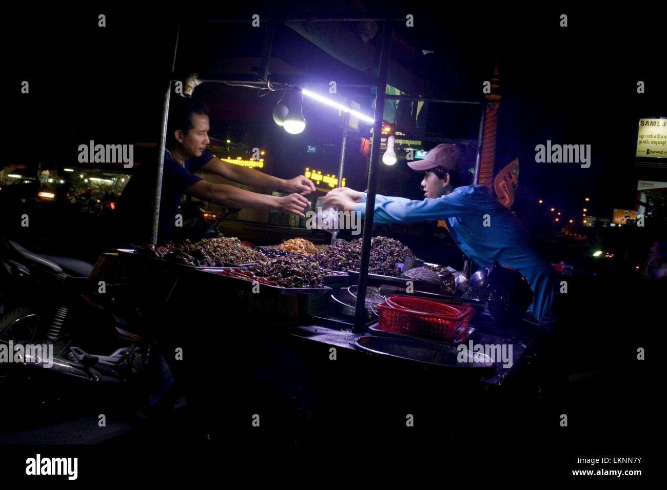 Un uomo è la vendita di fritte di insetti come cibo di strada di notte su una strada di città in Kampong Cham, Cambogia. Foto Stock
