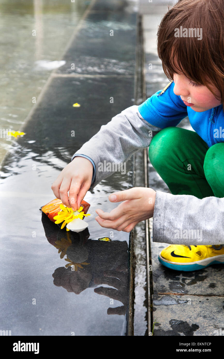 6 anno vecchio ragazzo facendo una barca da un scartato può e fiore. Foto Stock