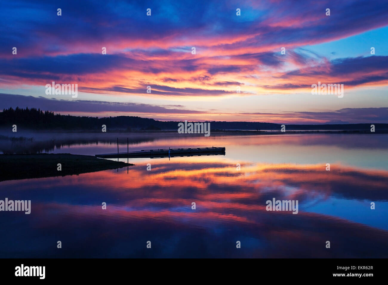 Un dock su di un lago calmo al tramonto. Foto Stock