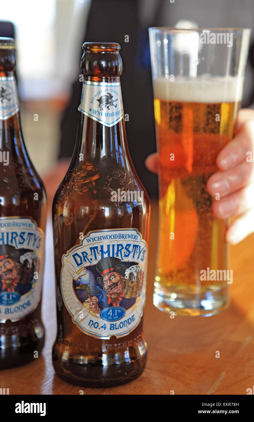 Bottiglie e un mans mano sollevare un bicchiere di Dr assetati di birra bionda da Wychwood Brewery Foto Stock