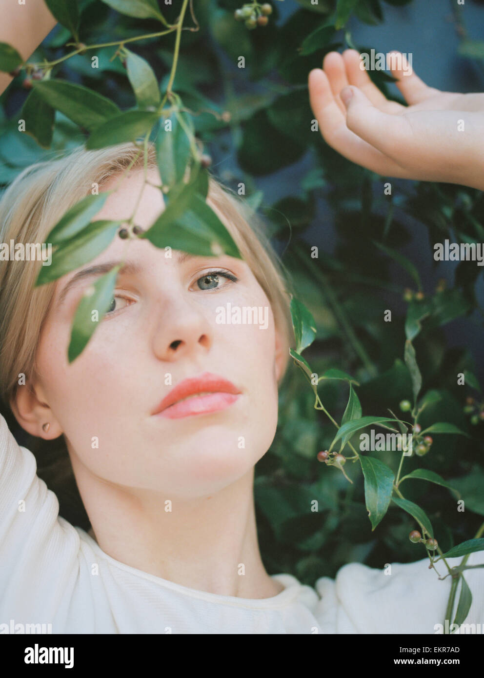 Una bionda donna dai capelli cercando wistfully attraverso una vite con foglie verdi. Foto Stock