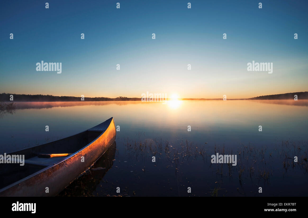 Una canoa su una calma piatta lago al tramonto. Foto Stock