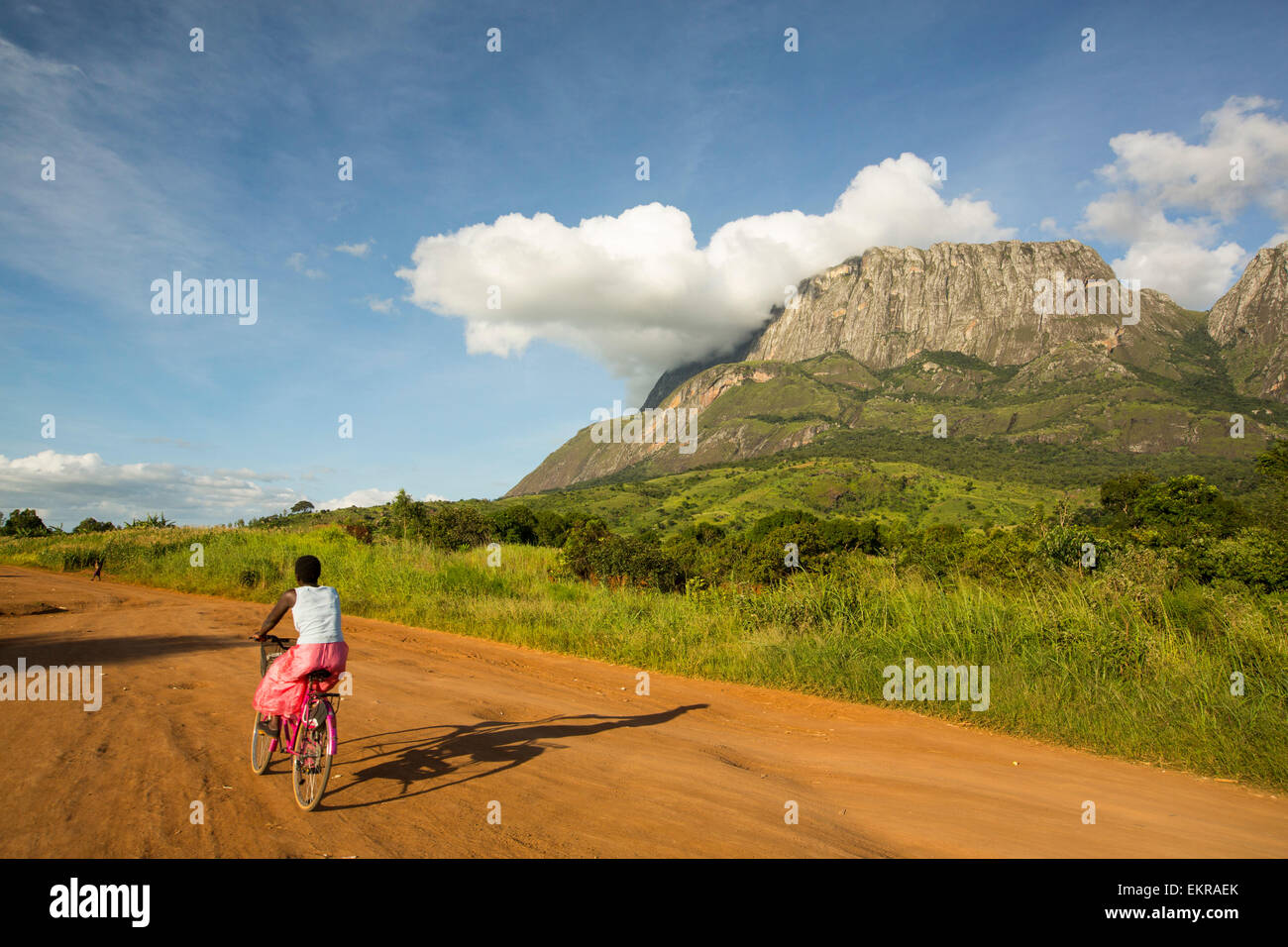 Una pista sterrata a Phalombe sotto il monte Mulanje in Malawi, Africa, con una donna su una bicicletta. Foto Stock