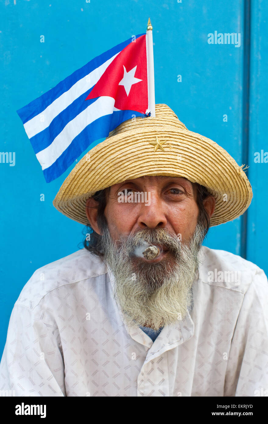 Un uomo cubano di fumare un sigaro sulle strade di l'Avana con una bandiera cubana nel suo cappello Foto Stock