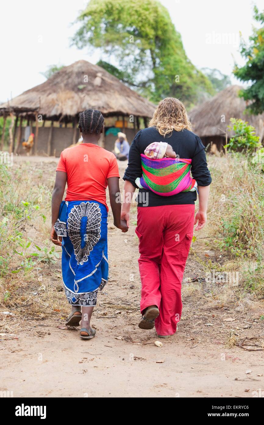 Due donne camminando insieme come una porta un bambino in una imbracatura; Manica, Mozambico, Africa Foto Stock