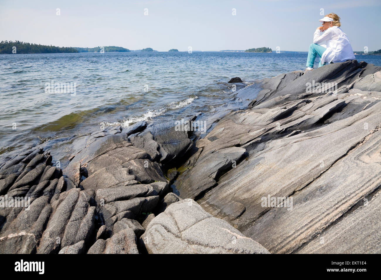 Donna seduta su una costa rocciosa che si affaccia su Georgian Bay a Killbear Parco Provinciale; Ontario, Canada Foto Stock