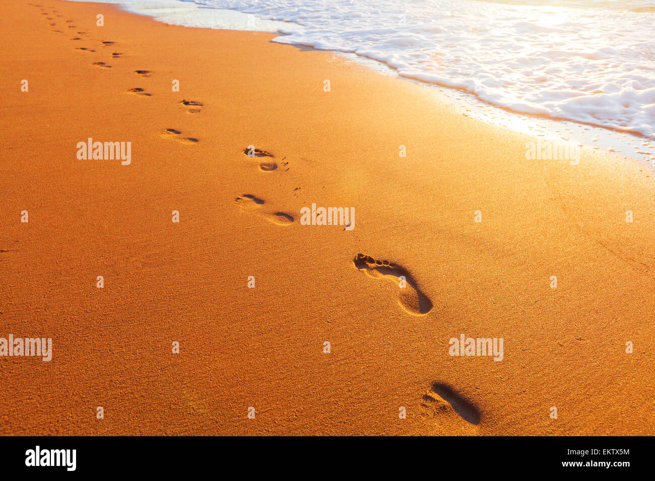 Spiaggia, onde e impronte in tempo al tramonto Foto Stock