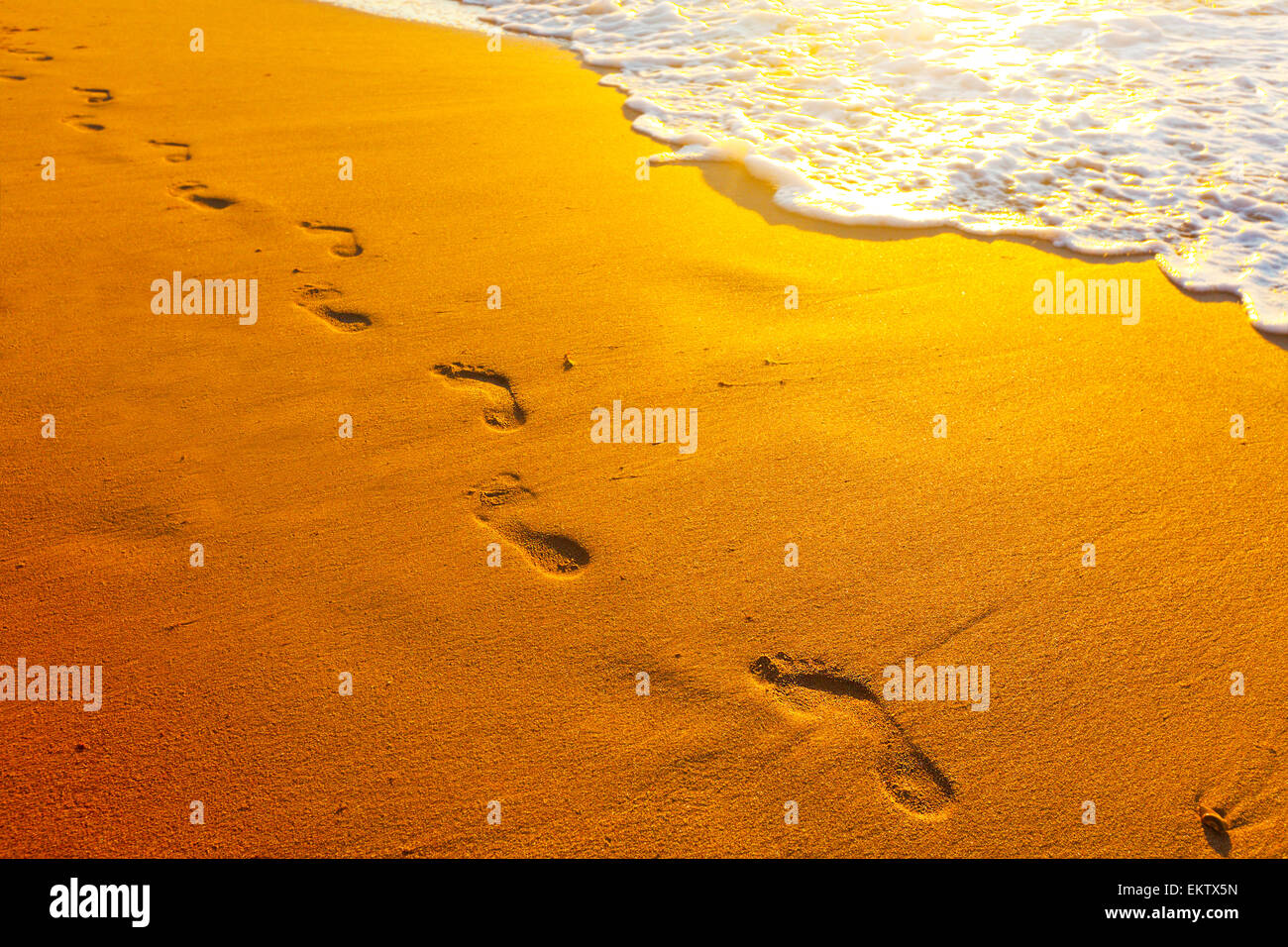 Spiaggia, onde e passi al tramonto Foto Stock