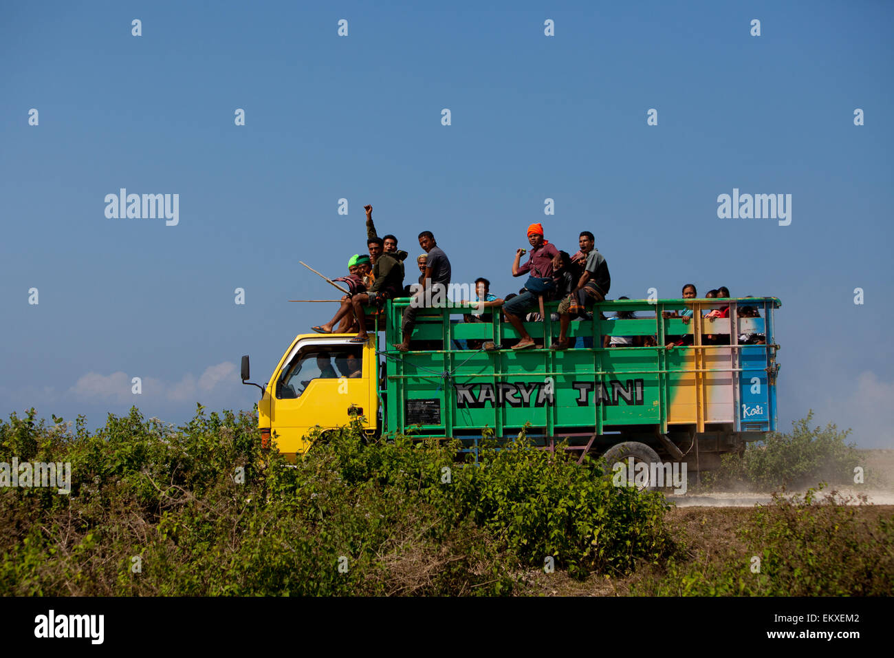 Le persone salutano mentre sono seduti su un camion che si sta muovendo su una polverosa strada rurale a Kodi, Southwest Sumba, Nusa Tenggara orientale, Indonesia. Foto Stock