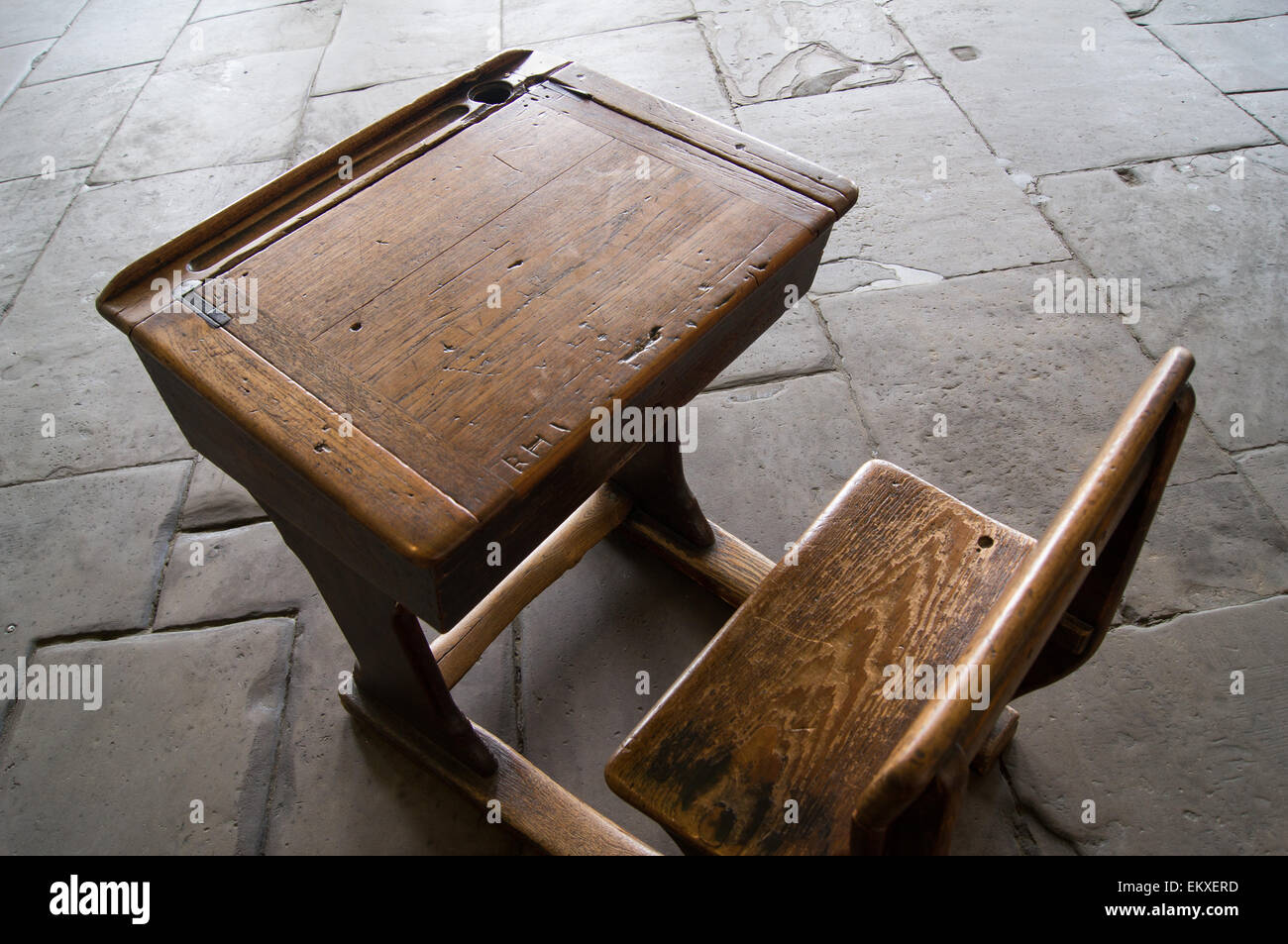 Un vecchio stile usurato scuola scrivania e sedia su un pavimento di pietra. Foto Stock