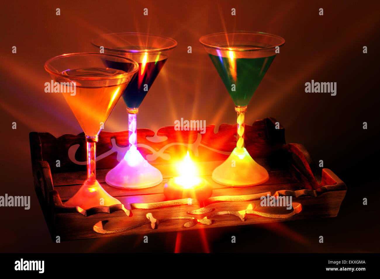 Un decorativamente vassoio intagliato con una candela e tre bicchieri da cocktail. Ciascuna lastra di vetro è illuminato dall'interno di una propria base da luci l.e.d. Foto Stock