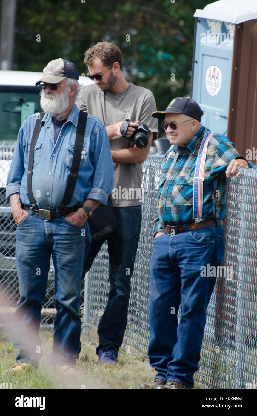 Tre uomini magra contro una recinzione mentre si guarda il bestiame concorsi al Blue Hill Fair, Maine. Foto Stock