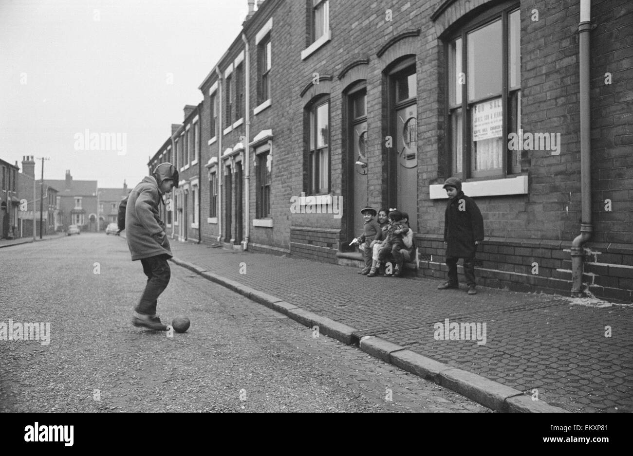 Due ragazzi asiatici giocando a calcio per strada mentre i loro amici guardare su Marshall Street Smethwick. 1 Dicembre 1964 - Foto Stock