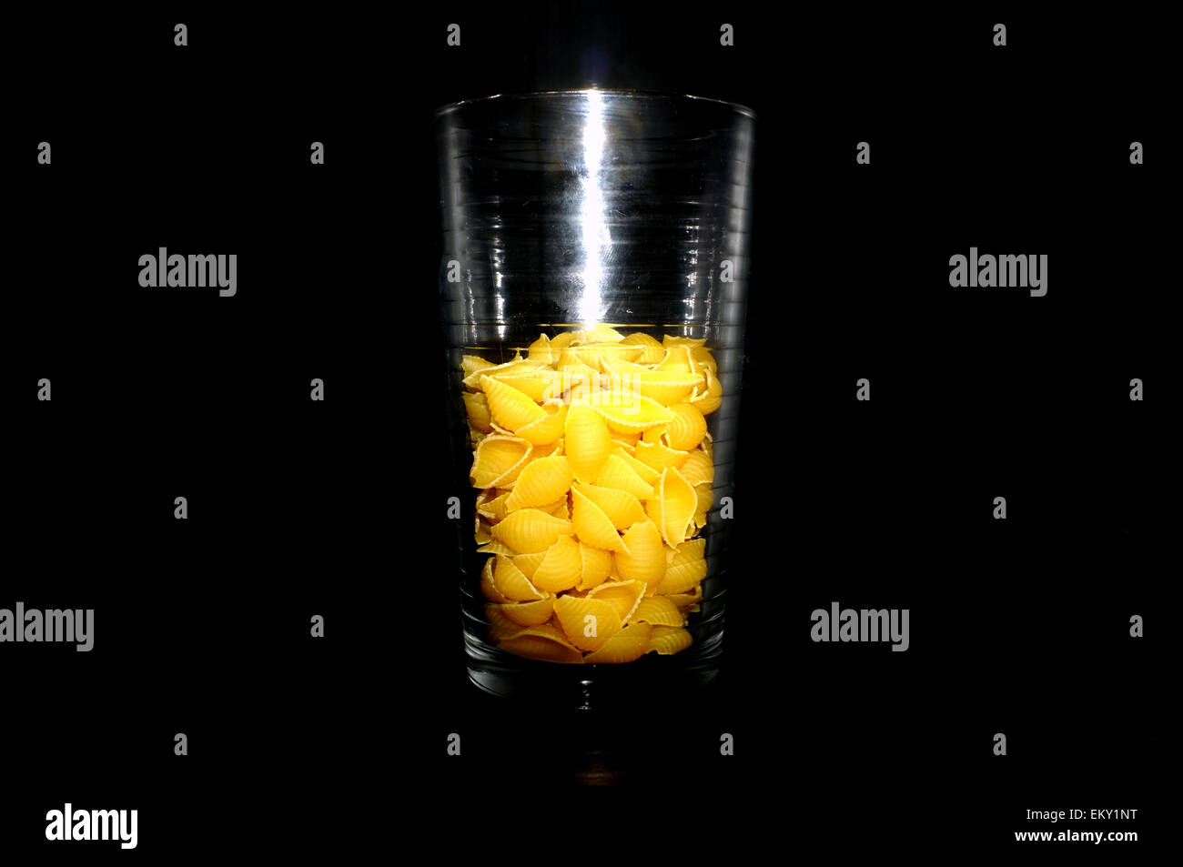 Un bicchiere mezzo pieno o mezzo vuoto di gusci di pasta contro uno sfondo nero. Foto Stock