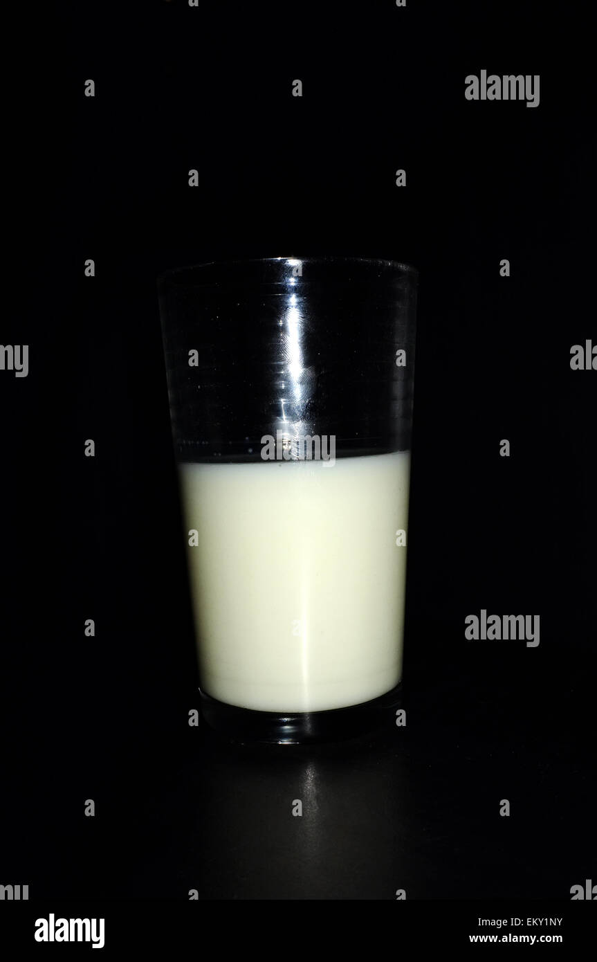 Un bicchiere mezzo pieno di latte fotografati contro uno sfondo nero. Foto Stock