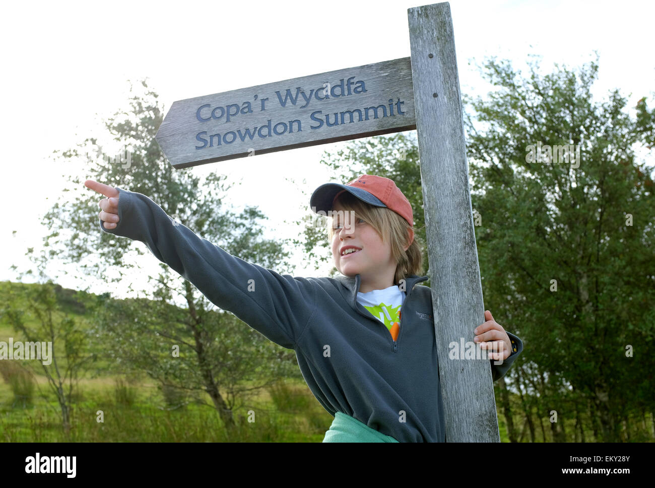 Un ragazzo si prepara a salire il monte Snowdon Snowdonia in piedi accanto al segno del percorso Foto Stock