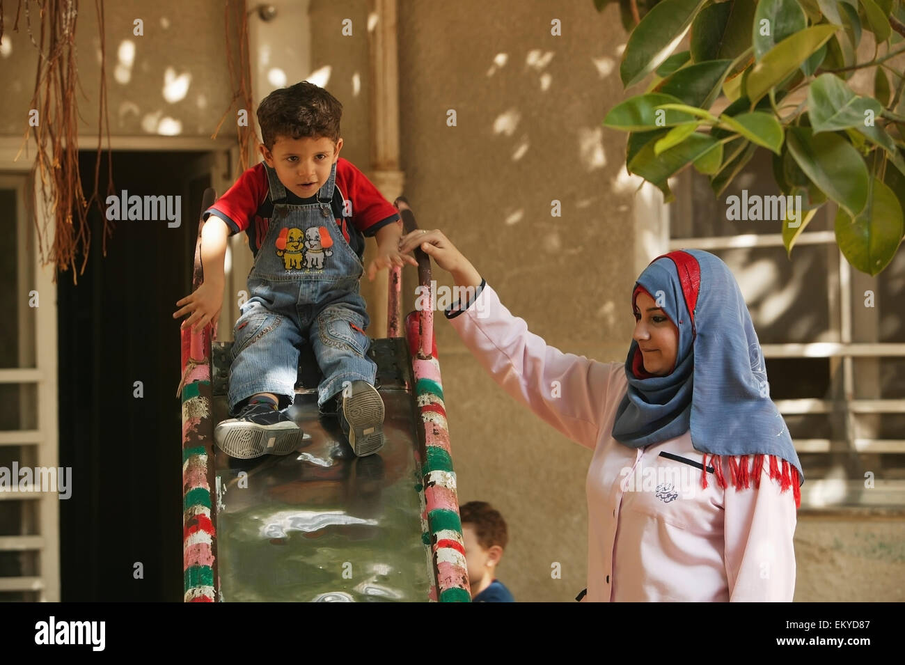 Un insegnante guida uno studente verso il basso una diapositiva alla sviluppo della prima infanzia europea; Alessandria, Egitto Foto Stock