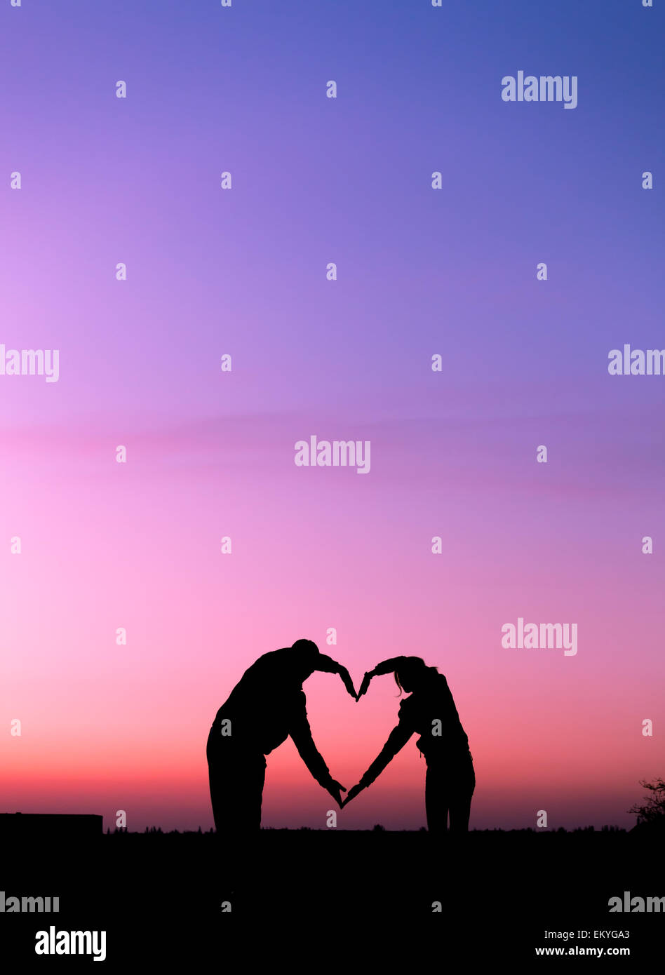 Cuore concettuale forma, simbolo dell'umano. Donna e uomo silhouette a mano oltre il cielo al tramonto sfondo, metafora per amore Foto Stock