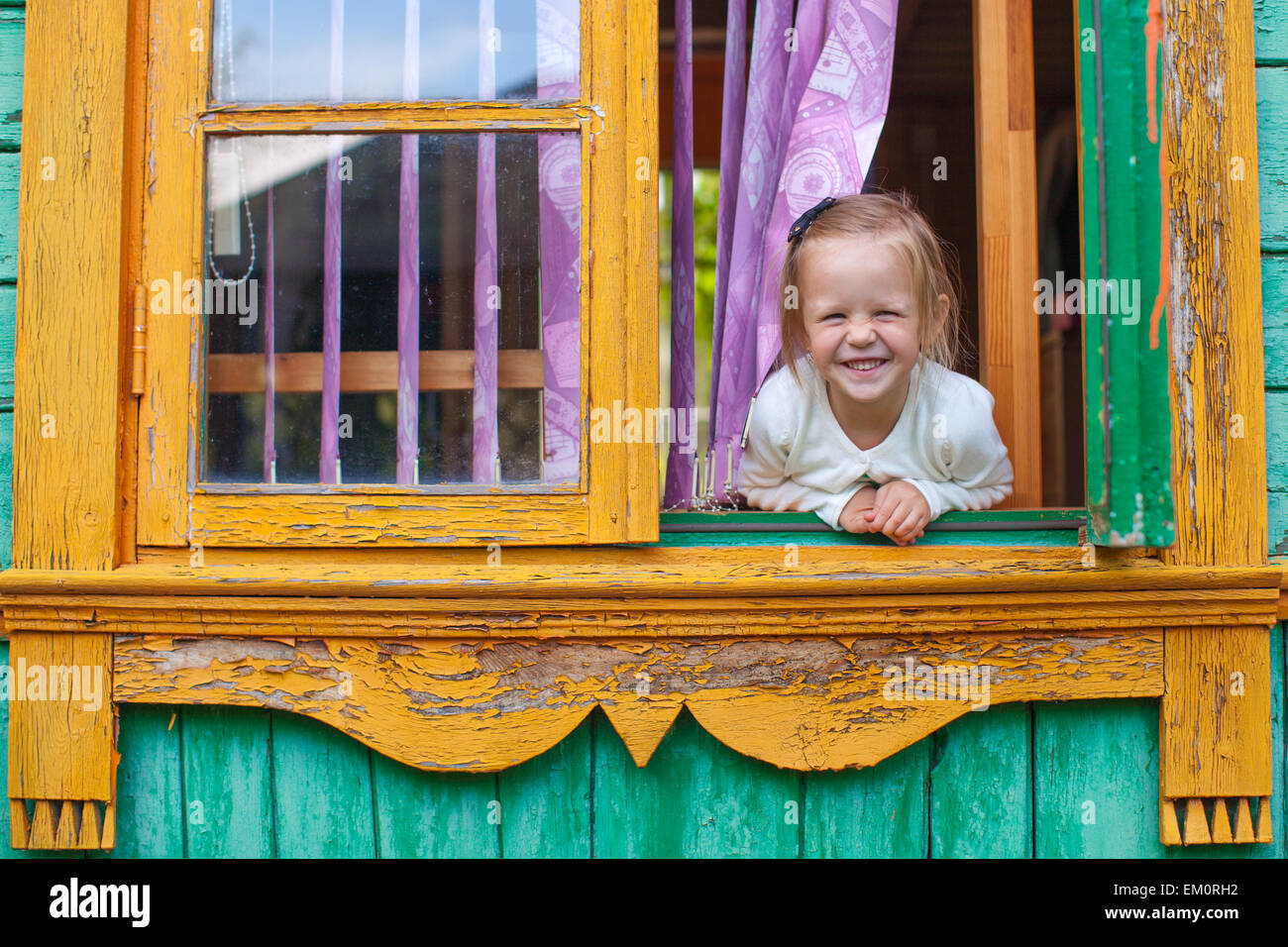 Adorabile bambina guarda fuori dalla finestra di casa rurale e risate Foto Stock