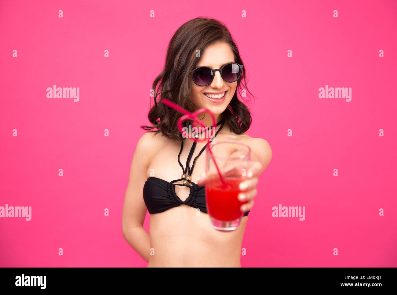 Donna felice in bikini dando il succo in telecamera su uno sfondo grigio Foto Stock