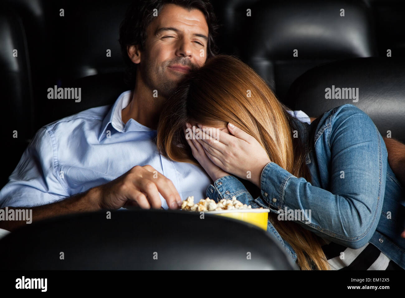 Frightened donna appoggiata sull'uomo nel cinema teatro Foto Stock