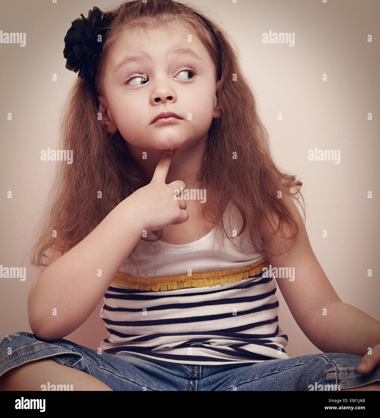 Il pensiero bambino indiscreti ragazza seduta in jeans con il dito sotto la faccia. Closeup ritratto vintage Foto Stock
