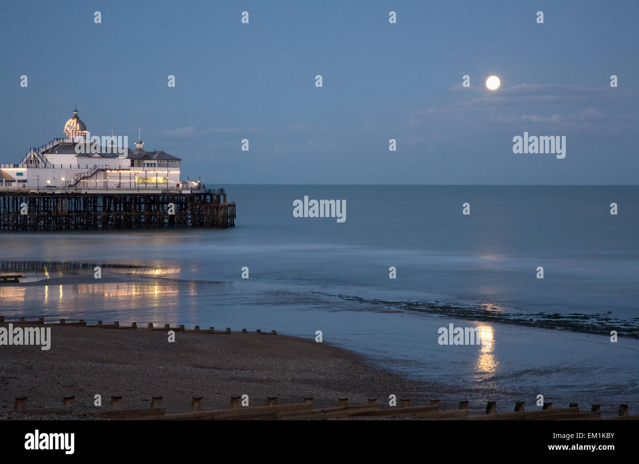 Edifici illuminati sul molo con una luna piena riflessa sulla spiaggia bagnata; Eastbourne Sussex England Foto Stock