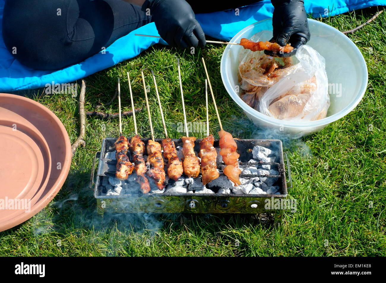 Una donna di cottura sate di pollo su un carbonaio su un glorioso pomeriggio soleggiato a Southsea common England Regno Unito Foto Stock