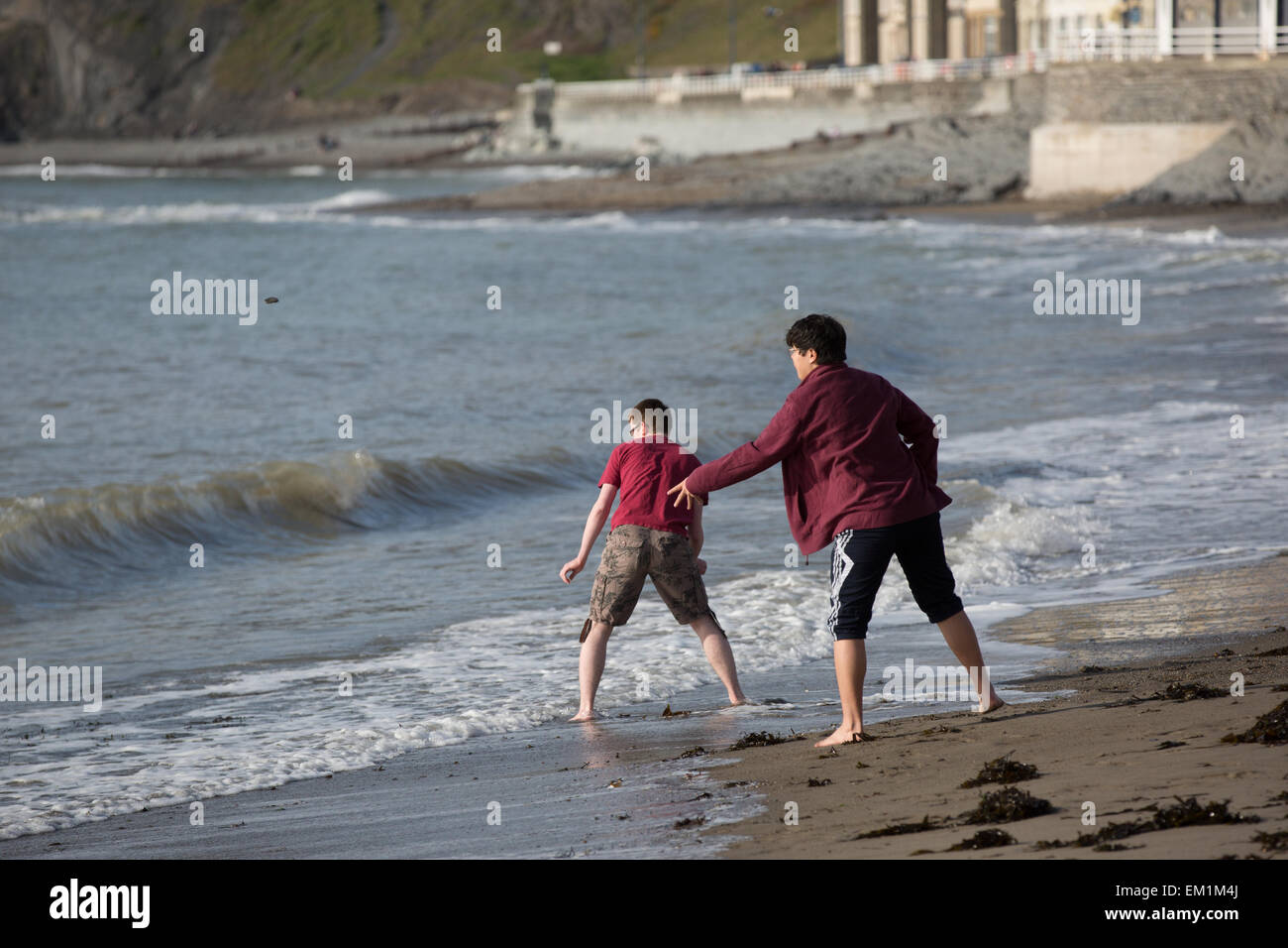 Aberystwyth, Wales, Regno Unito. Il 15 aprile 2015. Meteo. I giovani la scrematura di pietre sulle onde del sole Credito: Alan Hale/Alamy Live News Foto Stock