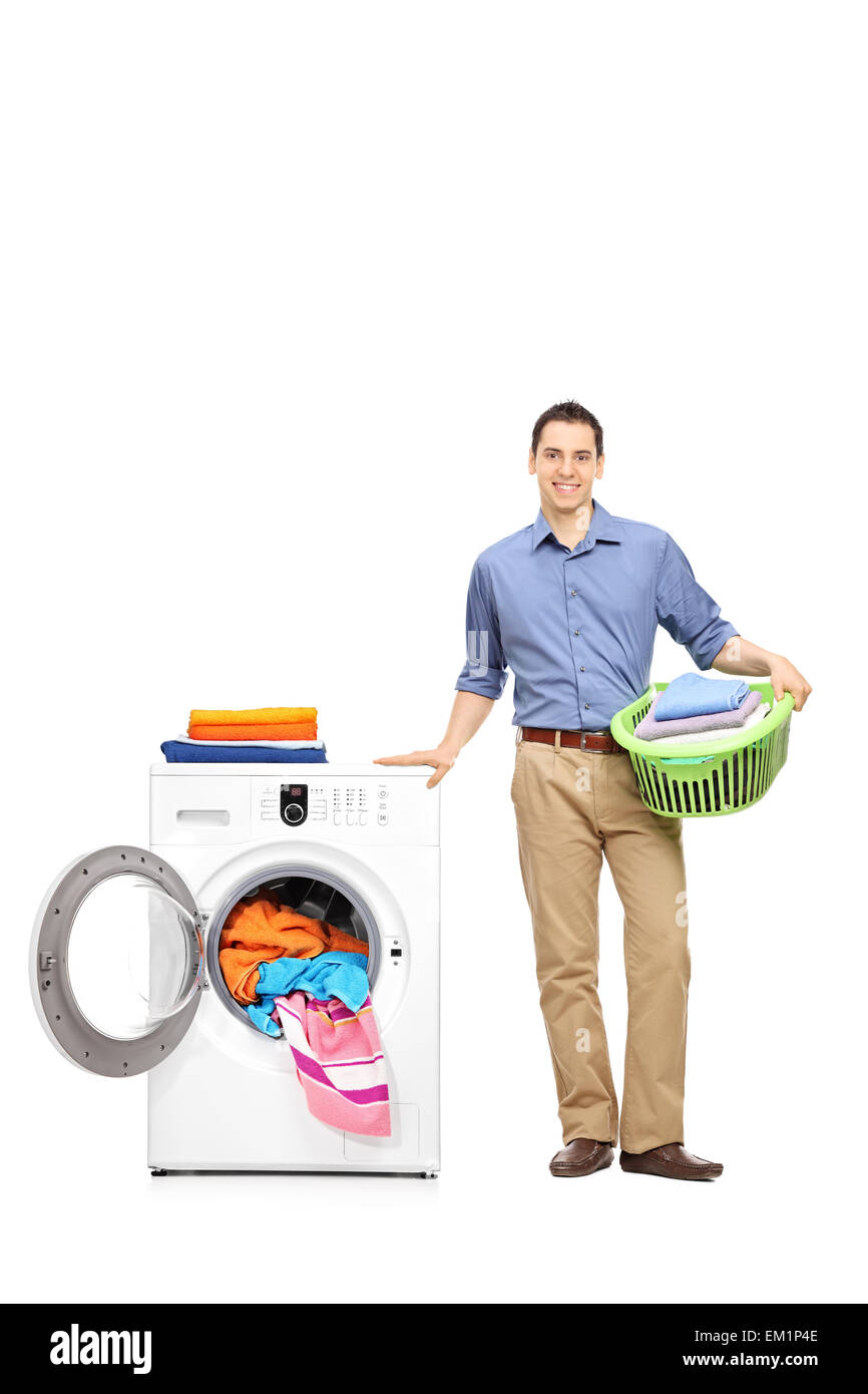 A piena lunghezza Ritratto di un giovane uomo in piedi accanto ad una macchina di lavaggio dei panni, tenendo un verde un cesto della biancheria Foto Stock