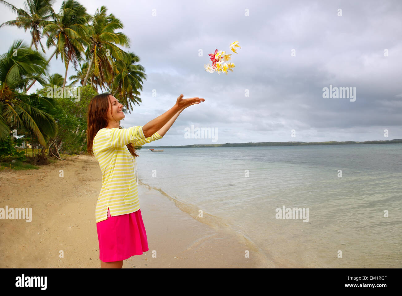 Giovane donna su una spiaggia di gettare i fiori in aria, Ofu island, Tonga Foto Stock