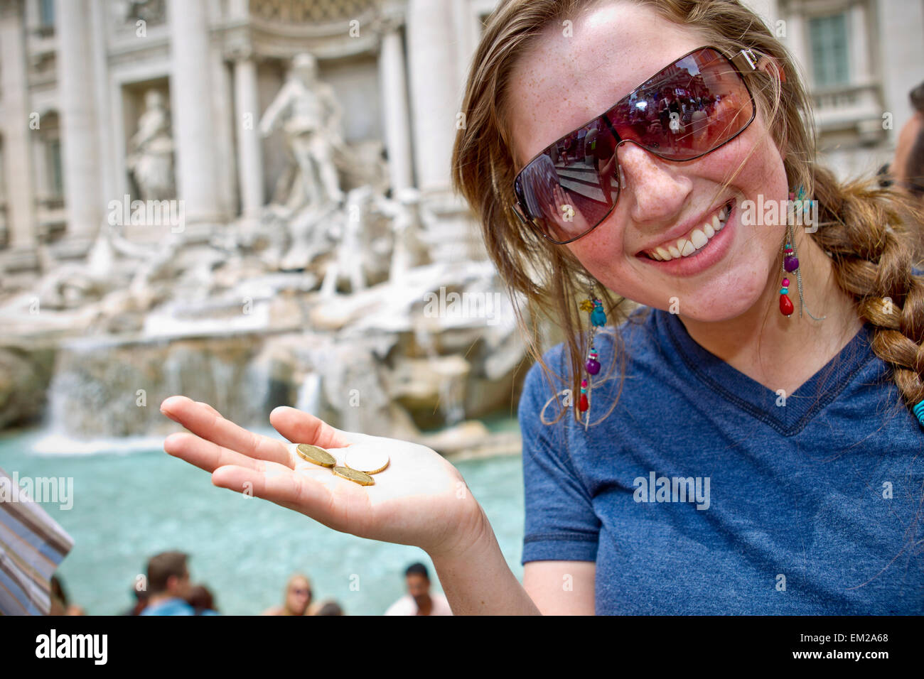 Una giovane donna contiene tre monete accanto alla Fontana di Trevi; Roma Italia Foto Stock