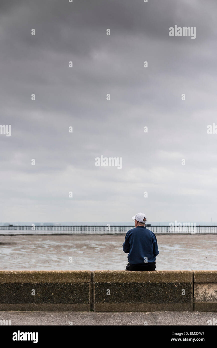 Un uomo seduto sul suo proprio sul lungomare di Southend in un giorno nuvoloso. Foto Stock