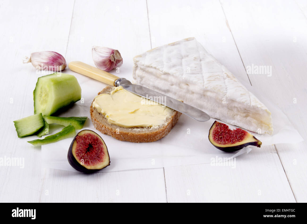 Il francese camembert, fetta di pane con burro, fig, aglio, coltello e pelate il cetriolo su carta bianca Foto Stock