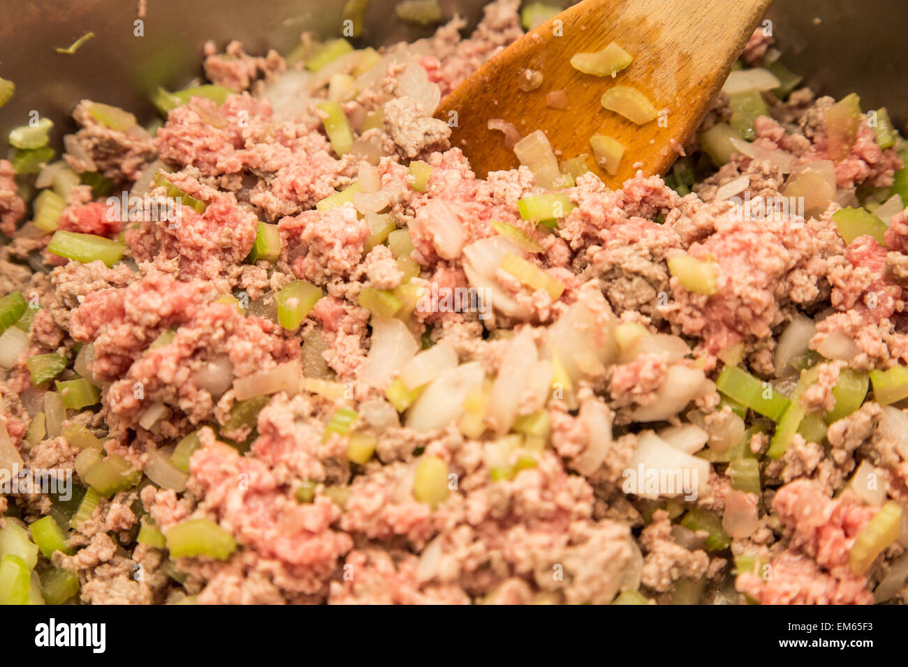 Cucinare la carne macinata, la cipolla tritata e il sedano in una padella con il cucchiaio di legno Foto Stock