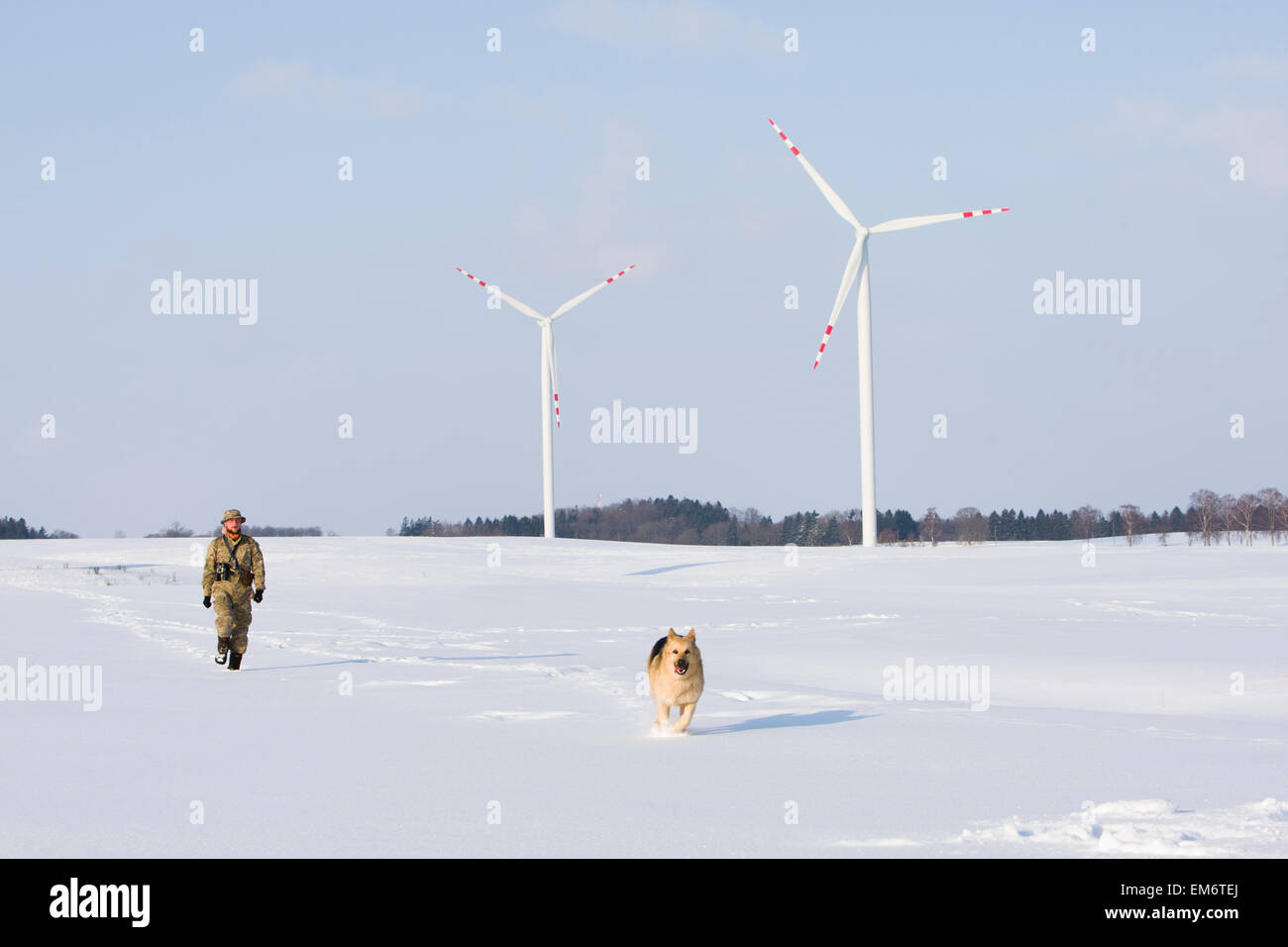 Un ornitholoigst, passeggiate attraverso la neve con il suo cane mentre cerca di uccelli a una fattoria eolica vicino Goscino, Polonia. Foto Stock