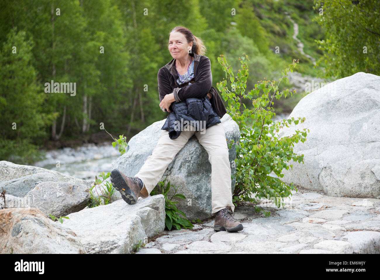 Una donna si rilassa su un macigno sulla banca del fiume Vénéon in La Bérarde, Hautes-Alpes, Francia. Foto Stock