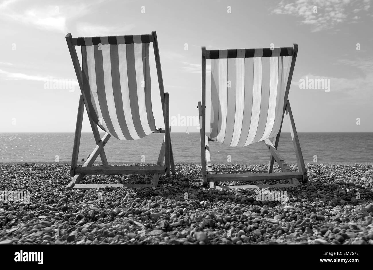 La spiaggia di Brighton, sedie a sdraio sulla spiaggia con la sola imbarcazione a vela in background in bianco e nero Foto Stock