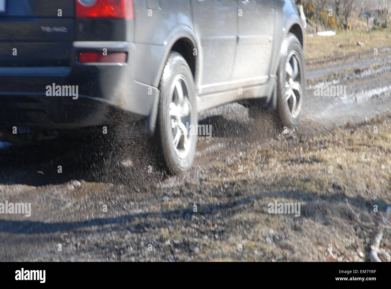 Le ruote delle auto spruzzano acqua guidando attraverso pozzanghere su strade fangose allagate. Foto Stock