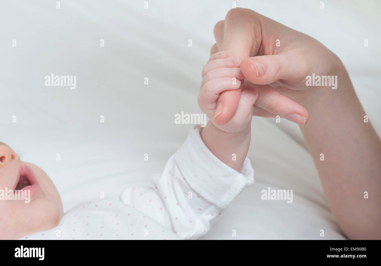 Baby girl azienda madre del dito sul letto Foto Stock