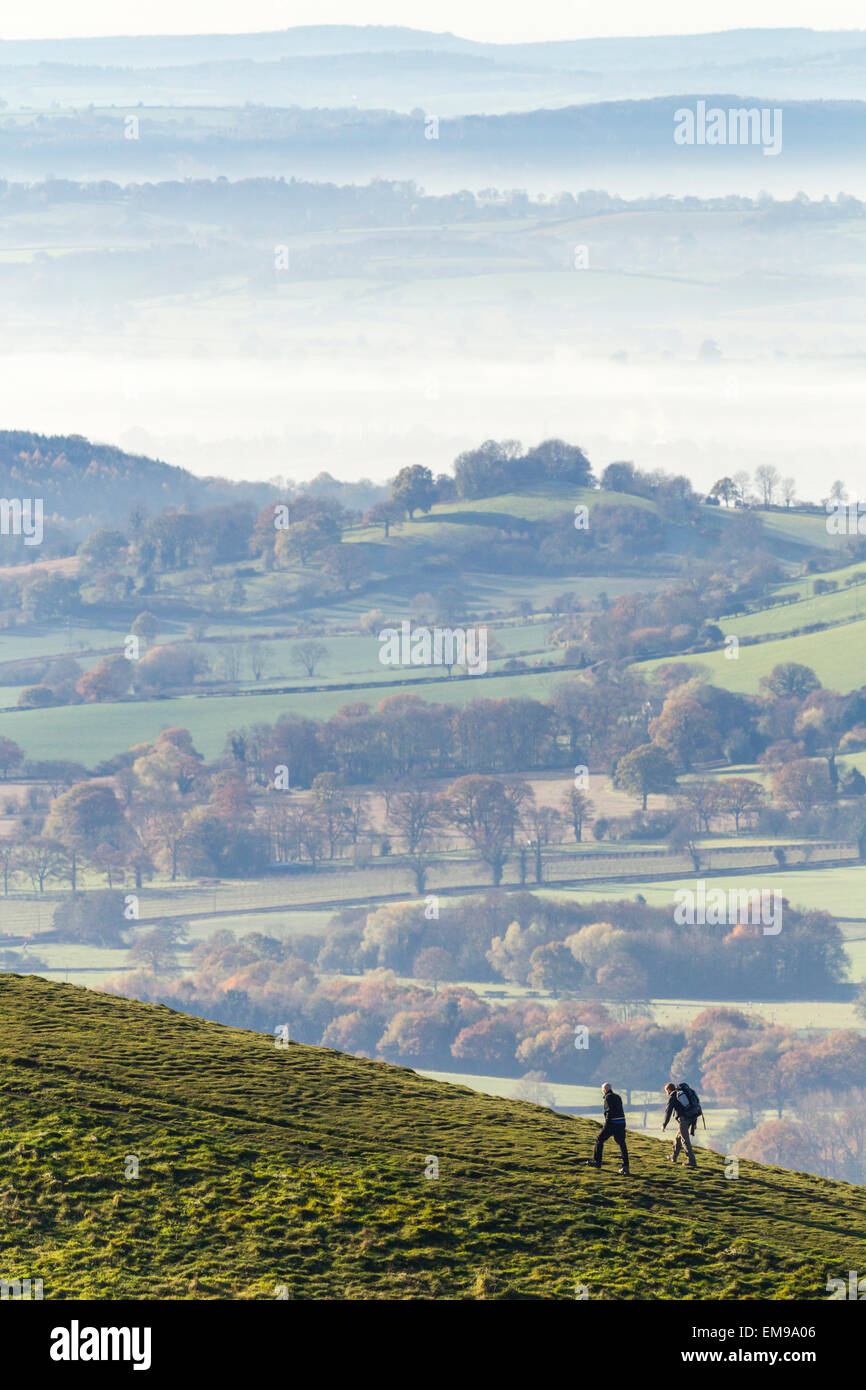 Due persone che camminano su Sugarloaf Hill su Malvern Hills con Hereford valle nella nebbia in background Foto Stock