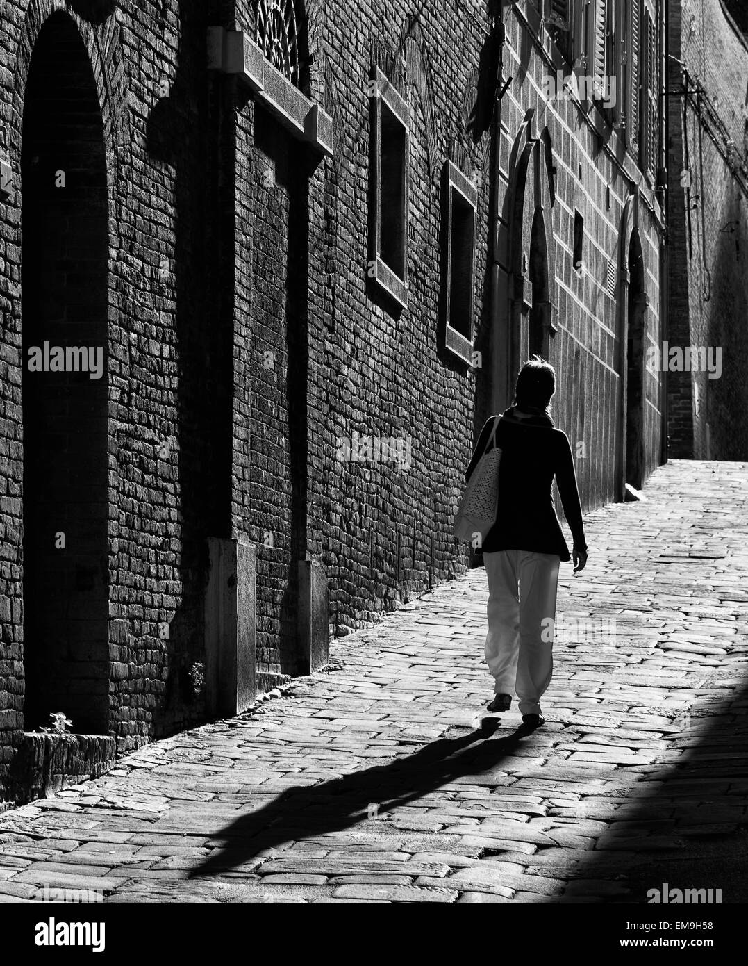 La donna a camminare su un sentiero acciottolato in Siena, Toscana, Italia Foto Stock