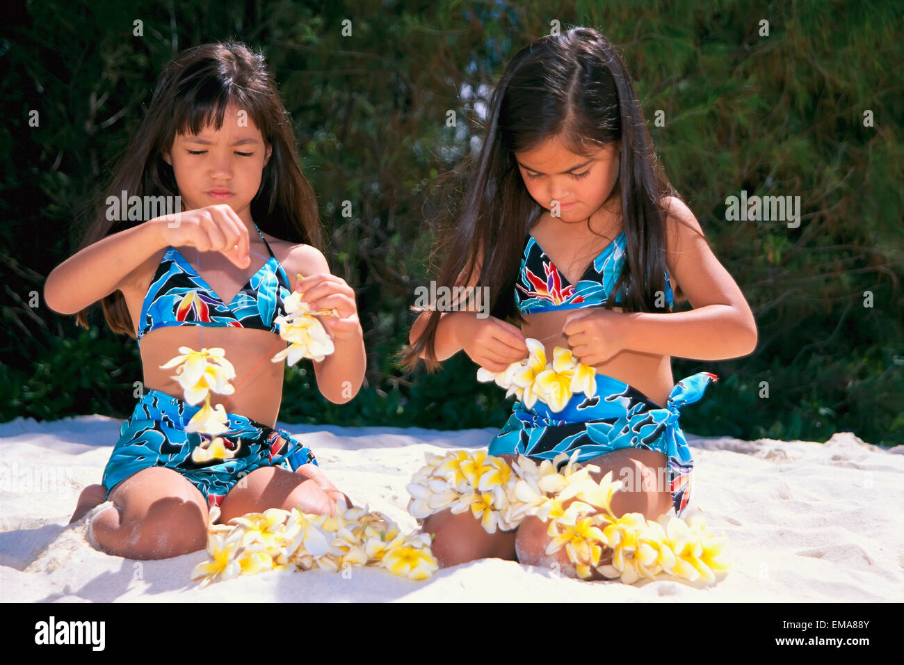 Pai di Hawaiian ragazze indossare abiti di corrispondenza sulla spiaggia, Stringing Plumeria fiori C1485 Foto Stock