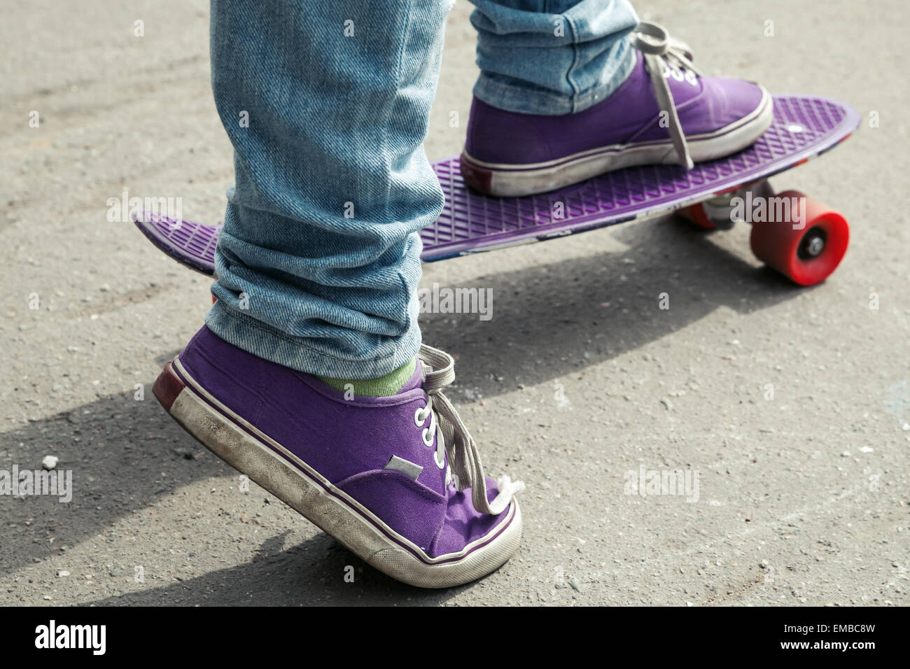 Giovane guidatore di skateboard in jeans in piedi sul suo pattino. Close-up frammento di skateboard e piedi Foto Stock