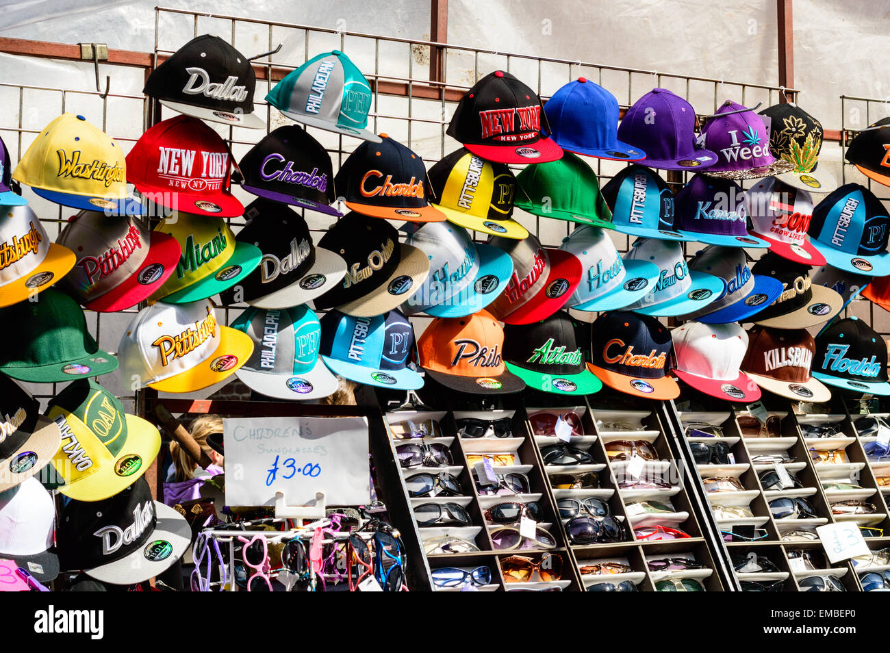 Righe di berretti da baseball e occhiali da sole per la vendita su un mercato in stallo a Whitby, North Yorkshire, Inghilterra. Foto Stock