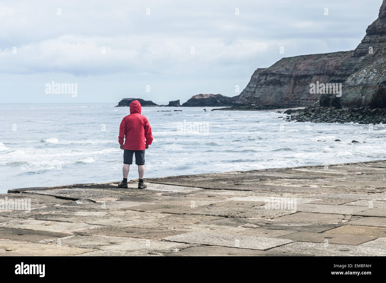 Non identificabili l uomo sta indossando cagoule rosso sul molo di cemento, a Whitby, North Yorkshire, Inghilterra. Foto Stock