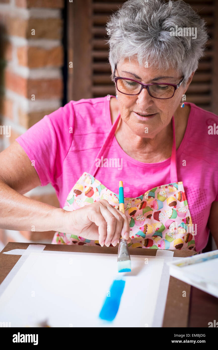 Una donna matura la spazzolatura blu il colore di sfondo per la sua pittura. Foto Stock